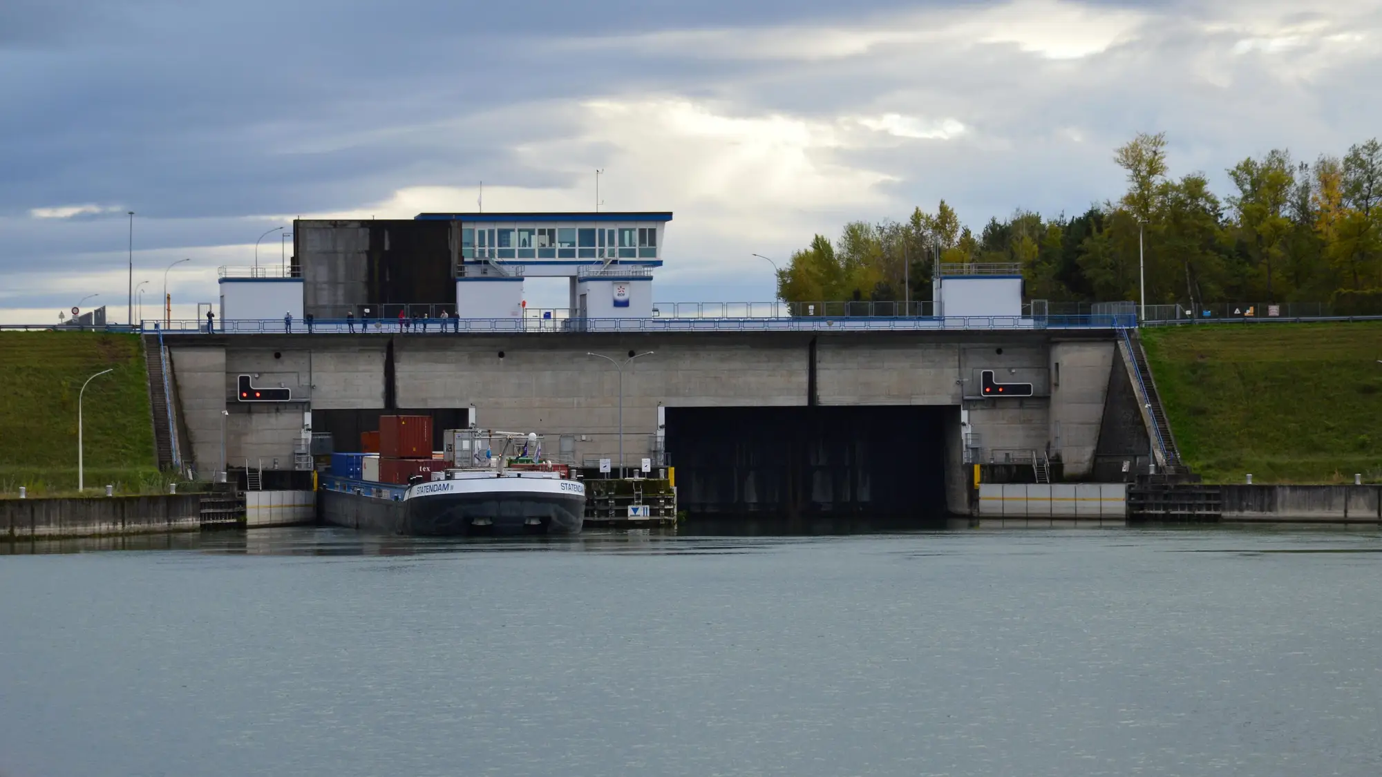 A loaded barge waiting below the gates of a concrete canal lock under a grey sky