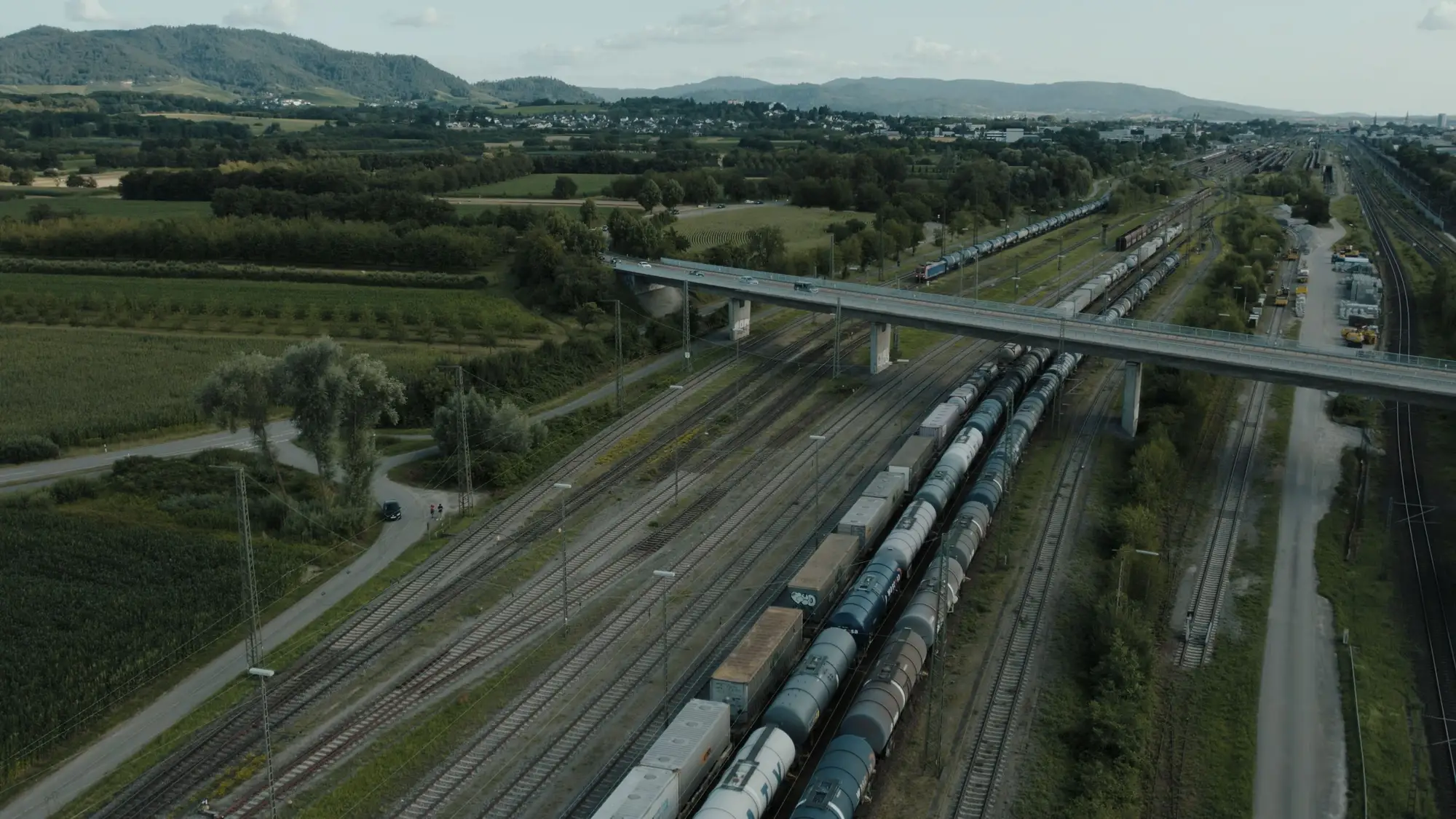 Freight wagons standing on parallel tracks in a rail yard beside a road bridge, seen from the air